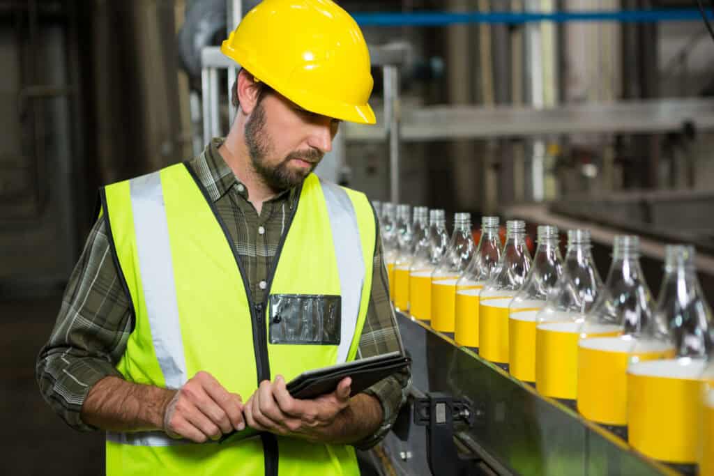 Male worker using digital tablet in juice factory to do quality control