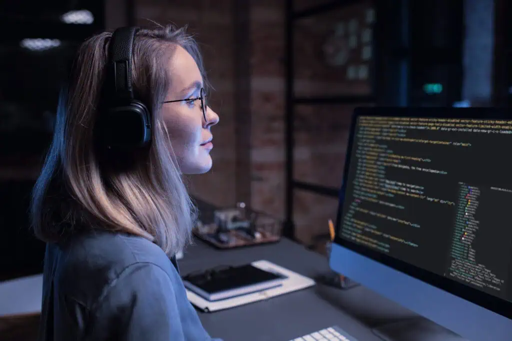 Female IT expert wearing headphones is coding on her computer