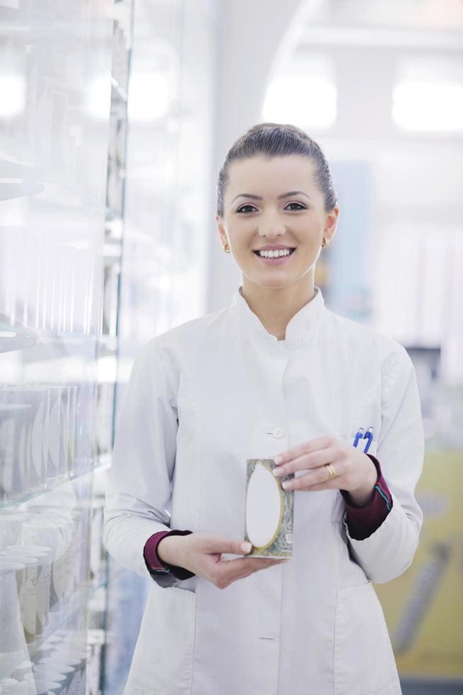 Woman in lab coat smiling while holding a sample in glass bottle